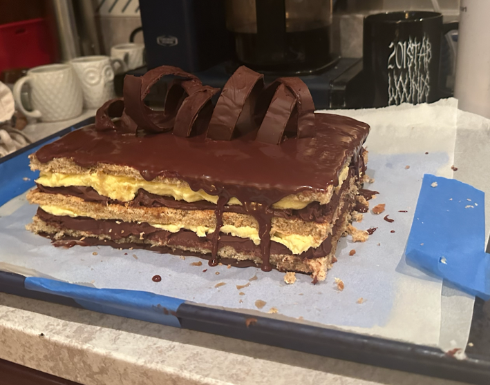 A completed opera cake that has not been trimmed, with dripping glaze and rough edges.